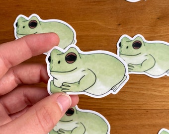 May include: A set of six green frog stickers with white outlines. The frogs are depicted in a cartoon style with large eyes and a smiling expression. The stickers are perfect for adding a touch of whimsy to any surface.