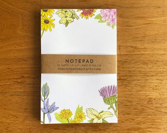 May include: A notepad with a floral design featuring a variety of flowers in shades of pink, purple, yellow, and green. The notepad has 50 sheets and measures 4" x 6". The text "NOTEPAD" is printed on the front of the notepad, along with the website "FERNINTHEFOREST.ETSY.COM".