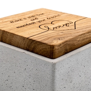 May include: A grey concrete box with a wooden lid. The lid has the text "Make a wish then manifest your dreams" and a heart with the text "love you" engraved on it.