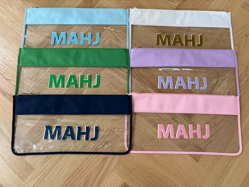 May include: Six rectangular zipper pouches with clear plastic bodies and colored fabric borders. Each pouch features the letters MAHJ in a matching color on the front. The colors include light blue, white, green, lavender, navy blue, and light pink.
