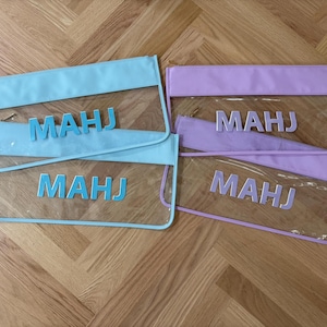 May include: Four rectangular zipper pouches made of clear plastic with colored borders and matching lettering. Two pouches feature light blue trim and the text "MAHJ" in light blue, while two feature lavender trim and the text "MAHJ" in lavender.