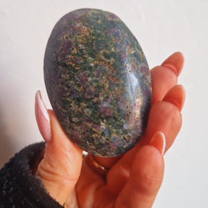 Peut inclure: Une pierre précieuse ovale avec un aspect moucheté. La pierre présente un mélange de teintes vertes, brunes et rouges, créant un motif unique et naturel. La surface polie reflète la lumière, soulignant la texture et les variations de couleur de la pierre.