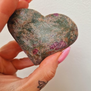May include: A heart-shaped green and pink stone with red ruby inclusions. The stone is polished and smooth.