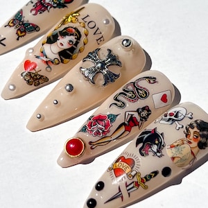 Puede incluir: Una colección de uñas artificiales en forma de almendra con varios diseños inspirados en tatuajes. Las uñas presentan imágenes de un diablo, mariposas, una mujer, una cruz, una serpiente, una rosa, una pin-up, una calavera, una pantera y la palabra "LOVE".