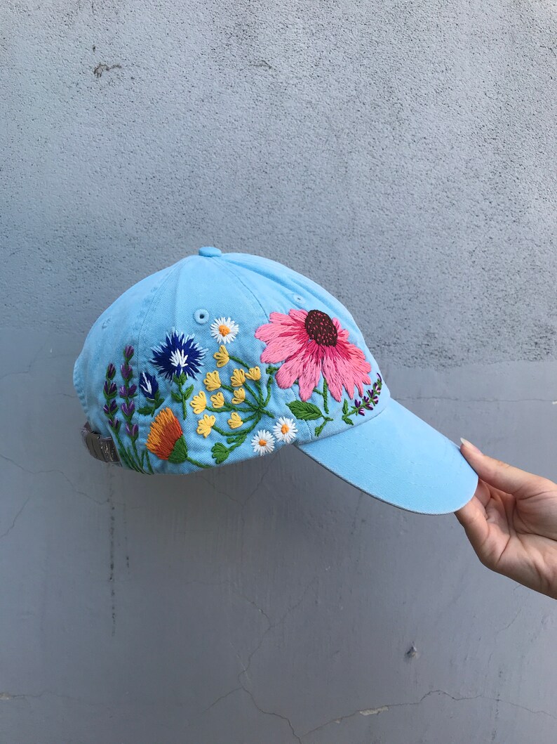 May include: A light blue baseball cap with embroidered flowers in shades of pink, yellow, orange, purple, and white.