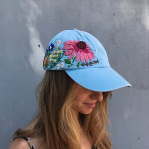 May include: A light blue baseball cap with embroidered flowers in pink, yellow, blue, and green.