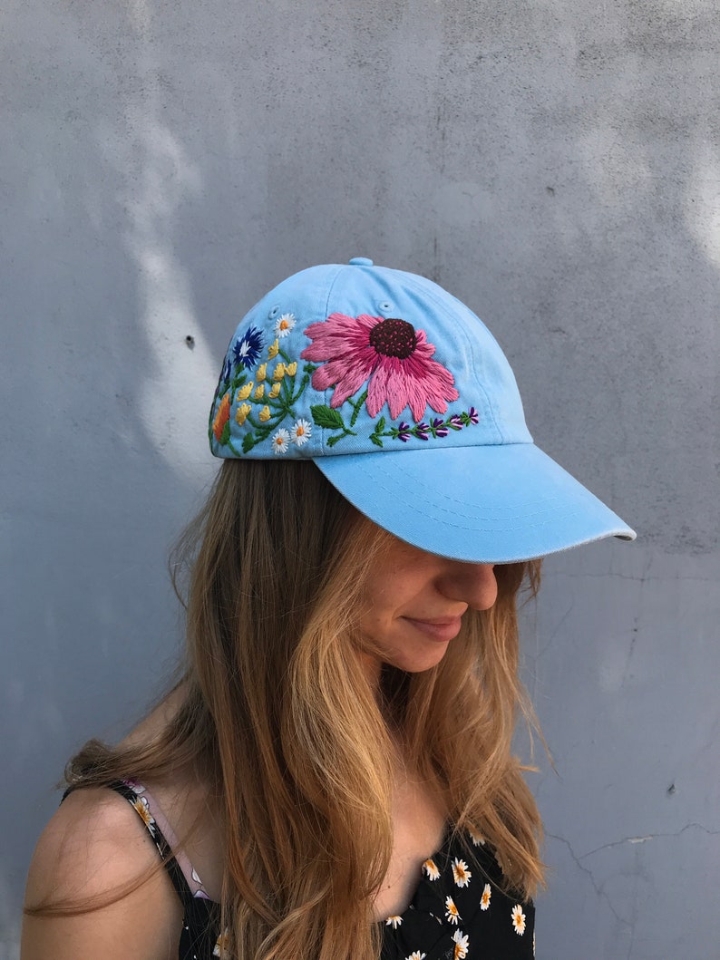 May include: A light blue baseball cap with embroidered flowers in pink, yellow, blue, and green.