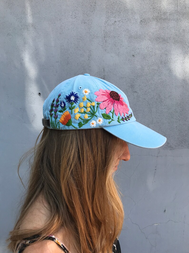 May include: A light blue baseball cap with embroidered flowers in shades of pink, orange, yellow, blue, and green.