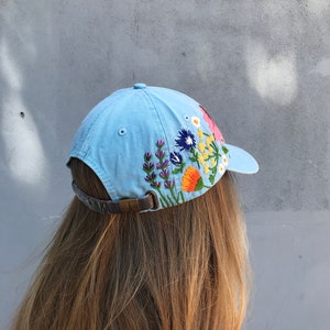 May include: A light blue baseball cap with embroidered flowers in shades of pink, yellow, orange, purple, and green.