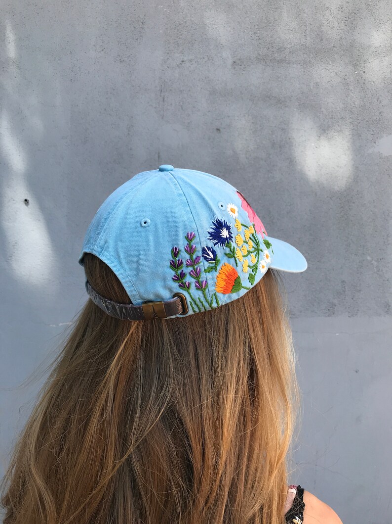 May include: A light blue baseball cap with embroidered flowers in shades of pink, yellow, orange, purple, and green.
