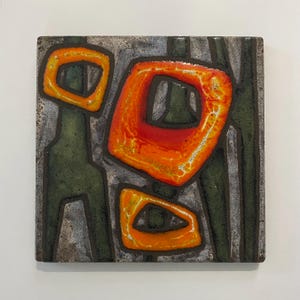 May include: A square ceramic tile featuring an abstract design with three prominent, glossy orange and red organic shapes outlined in dark brown. The background consists of textured, muted grey and dark green sections with a matte finish.