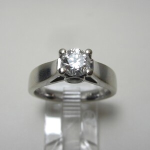 May include: A silver solitaire engagement ring with a round, clear diamond.