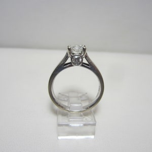 May include: A silver ring with a large round diamond in the center and two smaller round diamonds on either side.