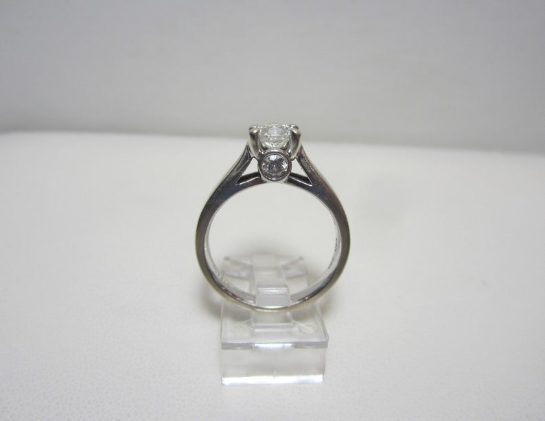 May include: A silver ring with a large round diamond in the center and two smaller round diamonds on either side.