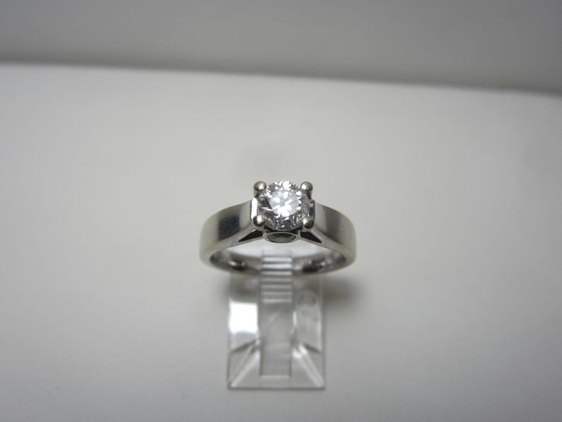 May include: A silver solitaire engagement ring with a round, clear diamond.