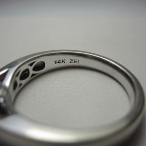May include: Close-up of the inside of a silver ring with the inscription "14K ZEI" on the band.