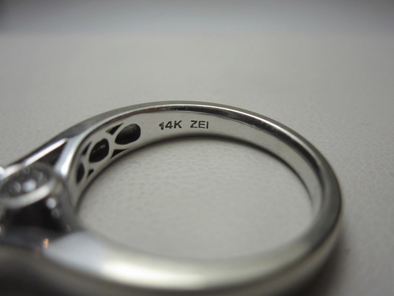 May include: Close-up of the inside of a silver ring with the inscription "14K ZEI" on the band.