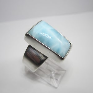 May include: A silver ring with a light blue rectangular gemstone. The gemstone has a swirling pattern.