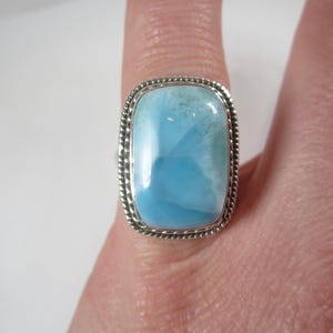May include: A silver ring with a large, light blue, rectangular, cabochon gemstone. The gemstone has a swirling, cloudy pattern.
