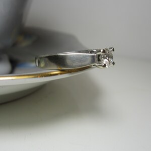 May include: A silver ring with a single, clear diamond set in a prong setting.