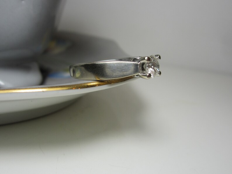 May include: A silver ring with a single, clear diamond set in a prong setting.