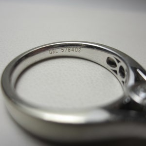 May include: Close-up of a silver ring with a diamond setting. The ring is engraved with the text "GSL 578402".
