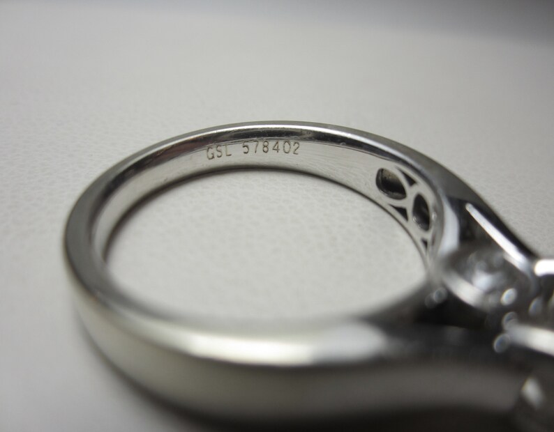 May include: Close-up of a silver ring with a diamond setting. The ring is engraved with the text "GSL 578402".