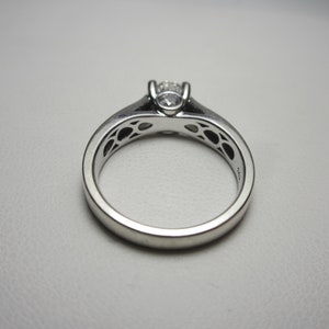 May include: A silver engagement ring with a single round diamond set in a prong setting. The band is decorated with a delicate filigree design.