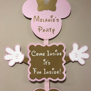May include: Pink and gold Minnie Mouse themed door hanger with white polka dots. The sign says "Come Inside It's Fun Inside!" and "Melanie's Party".