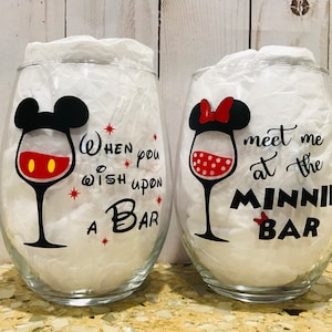 May include: Two wine glasses with Mickey Mouse and Minnie Mouse designs. The Mickey Mouse glass says "When you wish upon a bar" and the Minnie Mouse glass says "Meet me at the Minnie Bar".