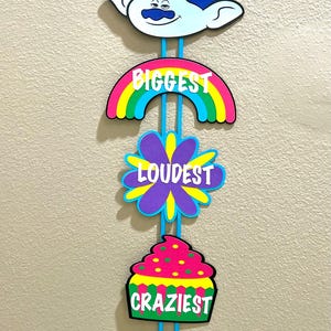 May include: A blue and white Trolls character cutout with the text "CLAY'S BIGGEST LOUDEST CRAZIEST PARTY" hanging from a blue ribbon.