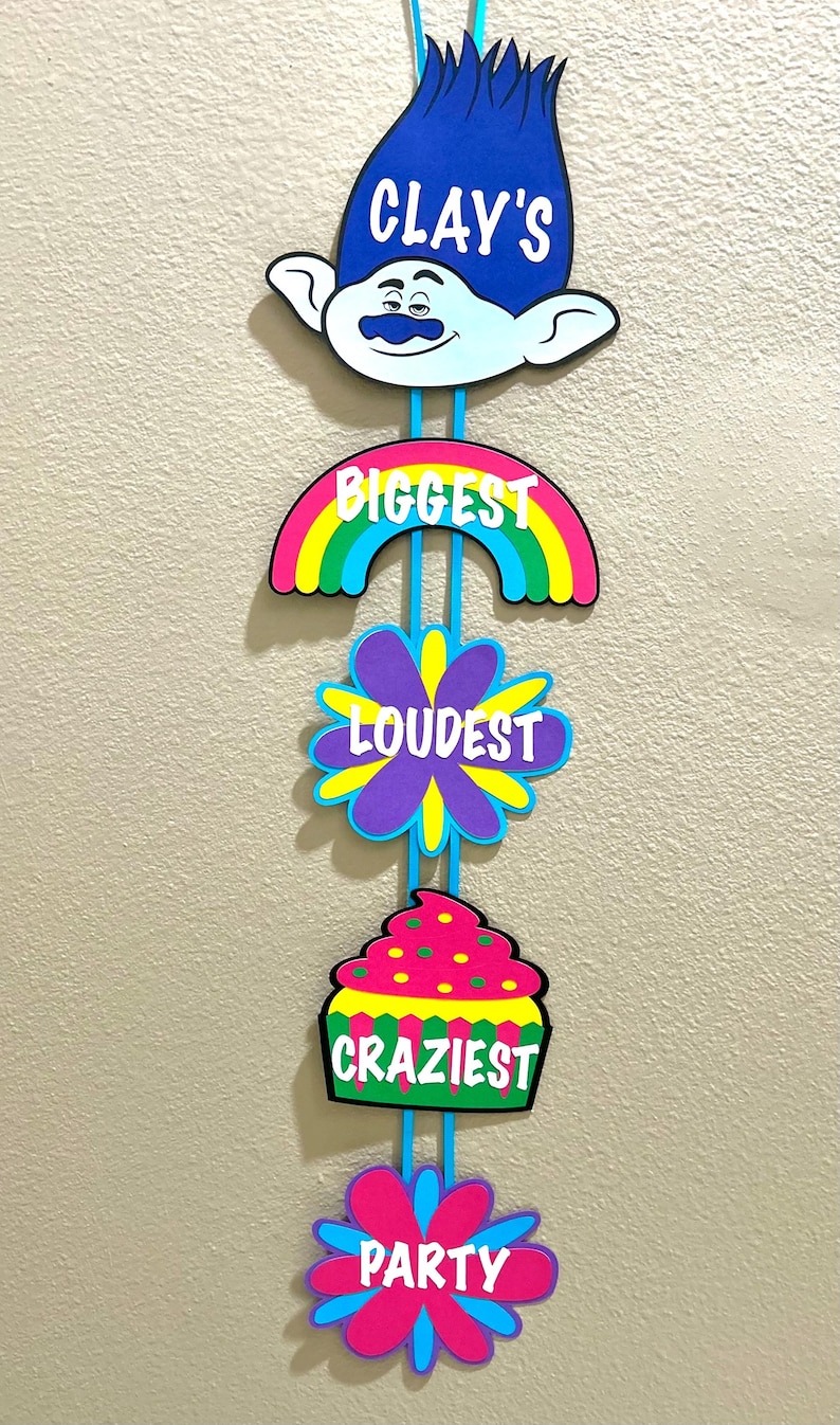 May include: A blue and white Trolls character cutout with the text "CLAY'S BIGGEST LOUDEST CRAZIEST PARTY" hanging from a blue ribbon.