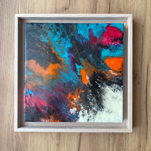 Puede incluir: Pintura abstracta en un marco de madera. La pintura presenta colores en espiral de azul, naranja, rojo y blanco.