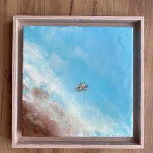 Puede incluir: Una pintura abstracta enmarcada con un fondo azul y remolinos blancos y marrones. Un pequeño barco amarillo se encuentra en el centro de la pintura.