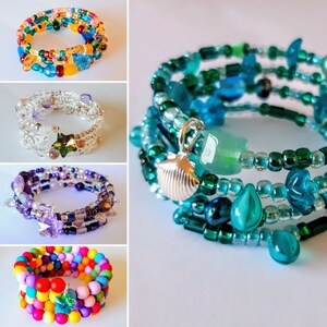 May include: Five colourful beaded bracelets with different charms. The bracelets are made with various colours of beads, including blue, green, purple, and rainbow. The charms include a seashell, a star, and a flower.