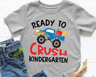 Puede incluir: Camiseta gris con un camión monstruo azul que lleva una manzana y un lápiz. El texto "Ready to Crush Kindergarten" está impreso en la camiseta.
