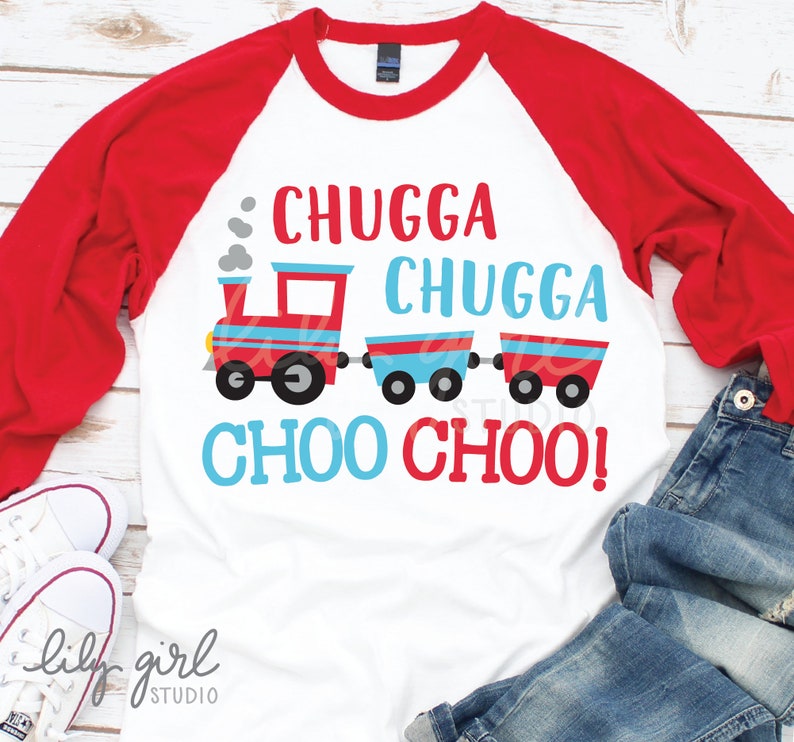 Pode incluir: Uma camiseta de beisebol de manga comprida branca com mangas vermelhas. A camiseta apresenta um trem de desenho animado vermelho, azul e branco com o texto "Chugga Chugga Choo Choo!" em vermelho e azul.