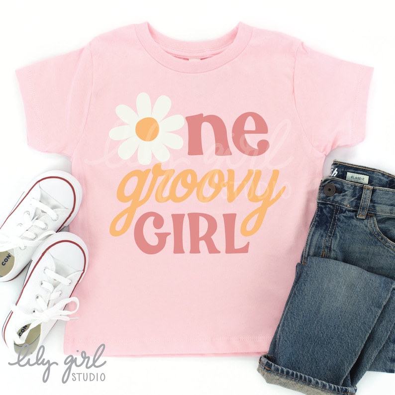 May include: Pink t-shirt with a white daisy and the text "one groovy girl" in orange and pink lettering.