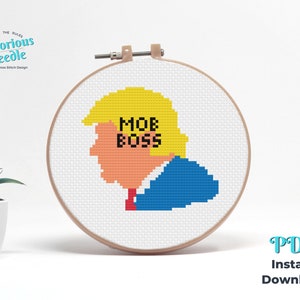 May include: Cross stitch pattern featuring a pixelated portrait of Donald Trump with the text "MOB BOSS" in black letters.