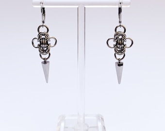 May include: A pair of silver earrings with a geometric design and a pointed tip hanging from each earring.