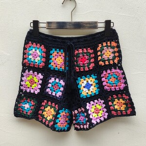 May include: Crochet shorts featuring a black base with a multi-colored granny square pattern. The shorts include a black drawstring waist and are constructed from individual square motifs in vibrant shades of pink, blue, yellow, orange, and green.