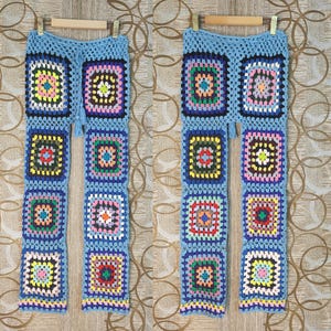 Könnte beinhalten: Eine blaue, gehäkelte Hose mit bunten quadratischen Mustern. Die Hose ist aus weichem, leichtem Garn gefertigt und hat eine lockere Passform.