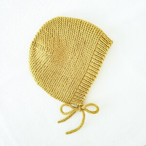 Puede incluir: Un gorro de bebé de punto amarillo con un lazo en la parte inferior.