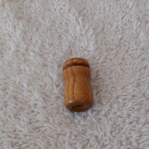 May include: A wooden pull for a window blind or shade. The pull is light brown with a darker brown band around the top.