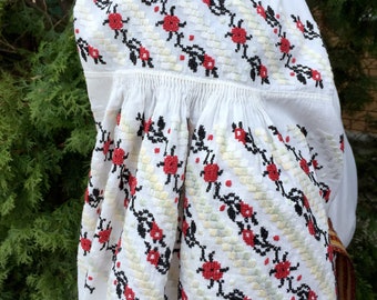 May include: White embroidered blouse with a black and red floral pattern. The embroidery is done in a cross-stitch style.