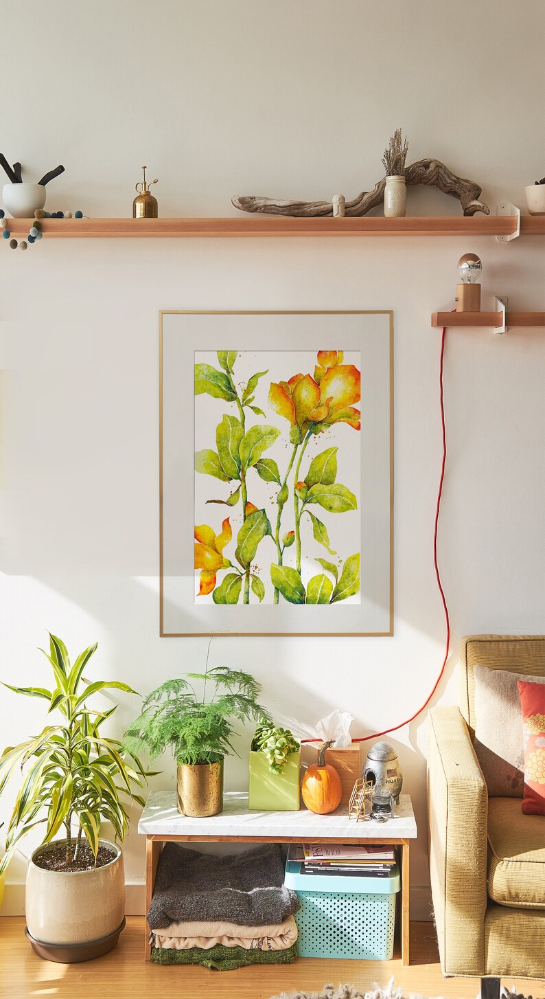 May include: A framed watercolor painting of yellow flowers with green leaves on a white background. The painting is hanging on a white wall above a wooden shelf with a small potted plant and a piece of driftwood. A couch with a throw pillow is in the foreground.