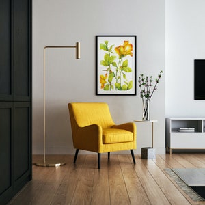 May include: A yellow armchair with black legs sits in a living room with a framed watercolor painting of yellow flowers, a floor lamp, and a white entertainment center with a television.