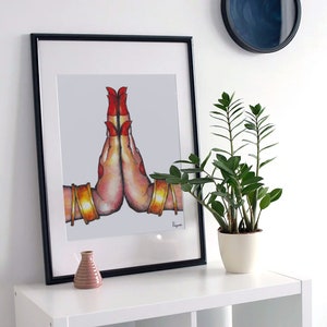 May include: A framed illustration of two hands in a prayer position, with red nail polish and gold bangles. The hands are on a white background.