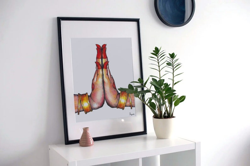 May include: A framed illustration of two hands in a prayer position, with red nail polish and gold bangles. The hands are on a white background.