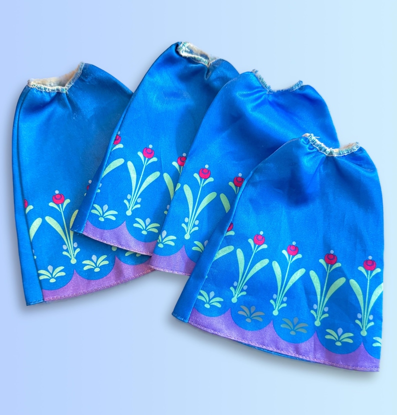 May include: Four blue satin doll skirts with a floral pattern in shades of green and pink. The skirts have a scalloped edge.